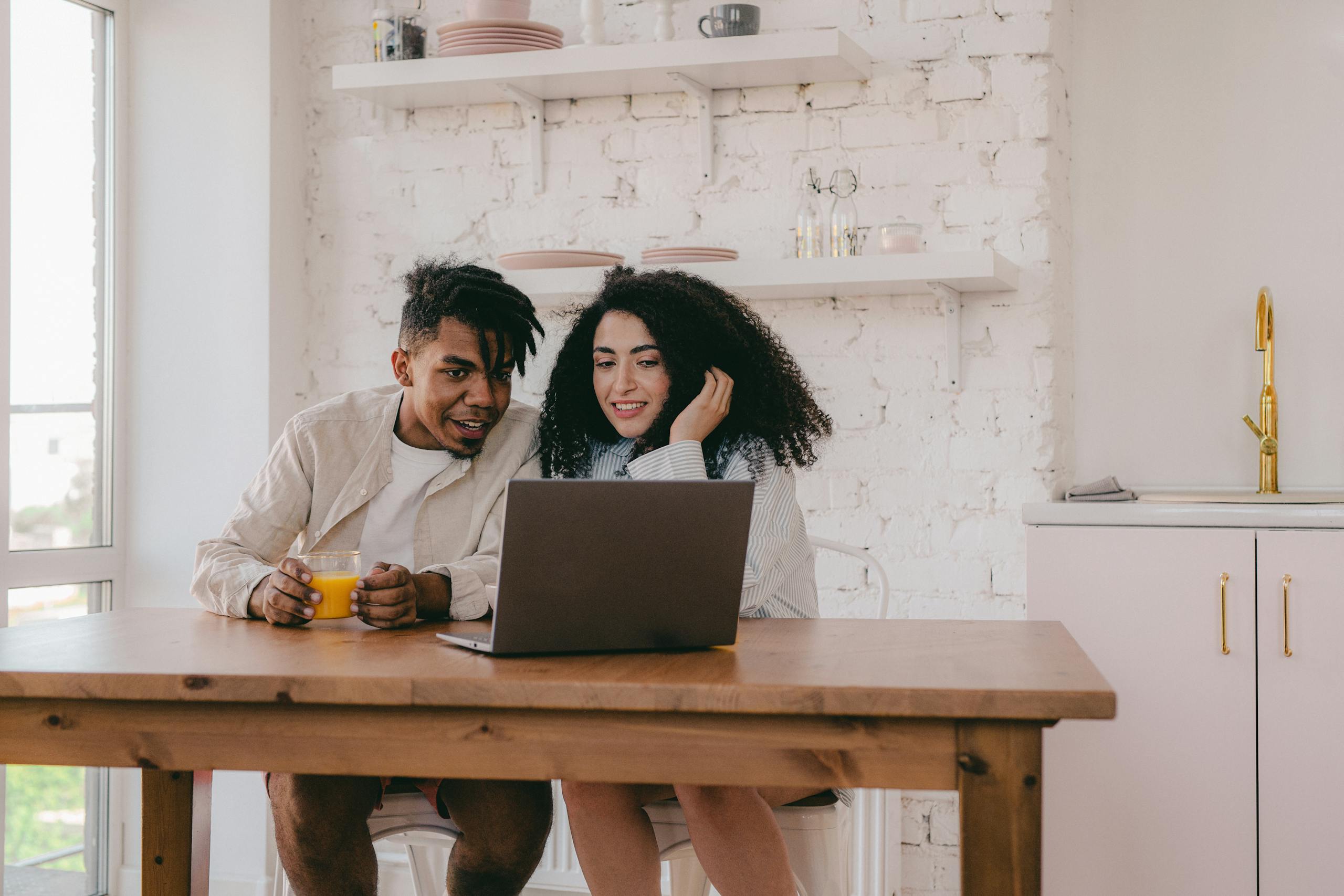 A cheerful couple sitting at a dining table, using a laptop in their cozy home.